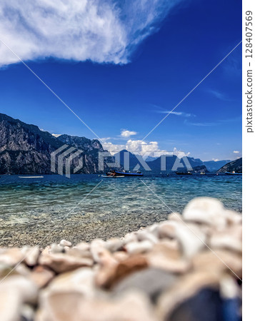 Crystal clear waters of Lake Garda with boats and scenic mountain backdrop. High quality photo 128407569
