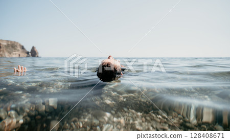 Woman swimming in sea at sunset, float on calm water back view. Concept of body image and fitness, enjoying a serene beach. Happy woman with perfect fit body enjoys sea beach 128408671