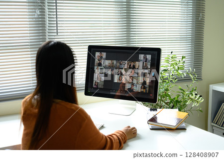 Rear view of young woman joining a team Zoom call on a desktop monitor Rear view of young woman joining a team Zoom call on a desktop monitor 128408907