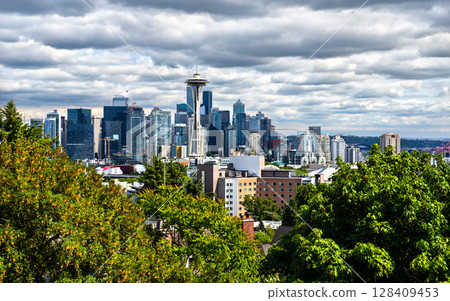 Iconic view of the Seattle skyline from Kerry Park with modern skyscrapers beneath a dramatic sky, framed by lush foreground trees Iconic view of the Seattle skyline from Kerry Park with modern skyscrapers beneath a dramatic sky, framed by lush foreground trees 128409453