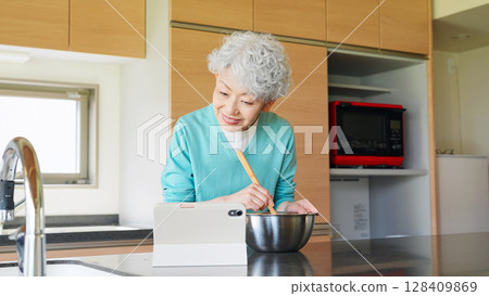 Senior woman cooking while looking at a tablet 128409869