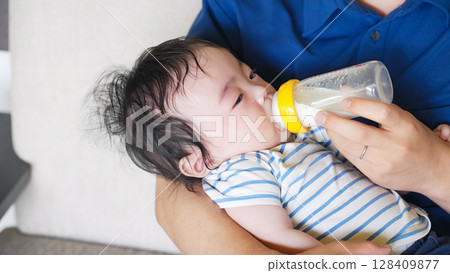 A man feeding a baby with a bottle A man feeding a baby with a bottle 128409877