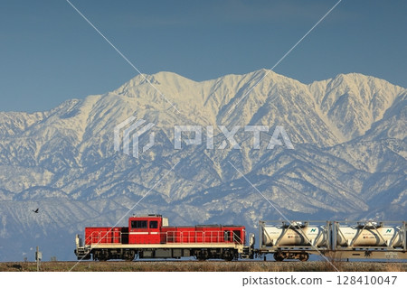 A freight train pulled by a DD200 diesel locomotive runs with the Tateyama mountain range in the background 128410047