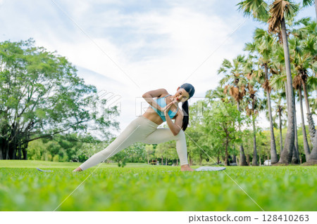 Asian woman practicing yoga outdoors in a peaceful green park 128410263