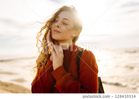 As she walked along the beach, the woman tourist adjusted her backpack, taking in the salty sea air As she walked along the beach, the woman tourist adjusted her backpack, taking in the salty sea air 128410314