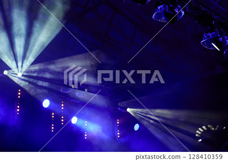 Stage with bright concert lighting, spotlights and smoke effects prepared for live music performance. Illumination for music event Stage with bright concert lighting, spotlights and smoke effects prepared for live music performance. Illumination for music event 128410359