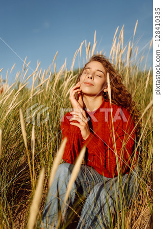 Beauty woman enjoying nature outdoors in grass. Calmness and tranquility. Travel, tourism concept. 128410385