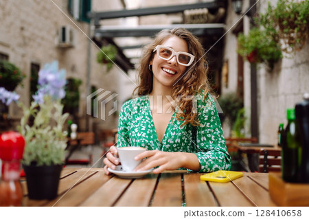 Young woman tourist drinks coffee in the old town in summer trip. People, fashion, lifestyle Young woman tourist drinks coffee in the old town in summer trip. People, fashion, lifestyle 128410658