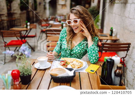 Portrait of a smiling woman eating pasta at cozy Italian restaurant outdoors. 128410705