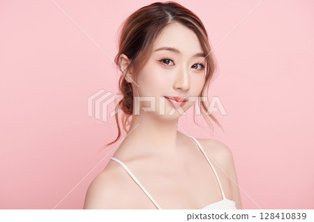 A beautiful young Asian woman with clean, fresh skin against a pink background. Skincare, facial treatment, cosmetology, beauty, and spa. An elegant portrait of an Asian woman. 128410839