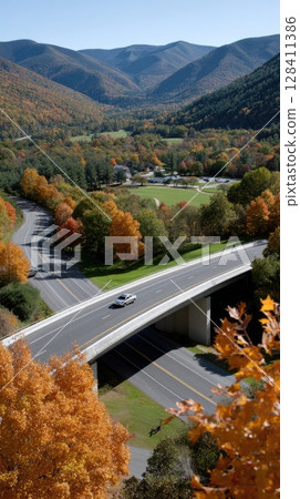 Colorful autumn leaves blanket the valley as a bridge spans the landscape, showcasing nature s beauty during the fall season Colorful autumn leaves blanket the valley as a bridge spans the landscape, showcasing nature s beauty during the fall season 128411386