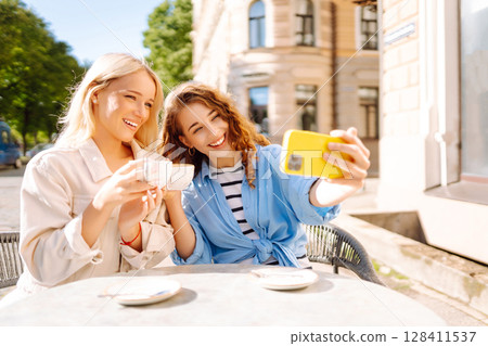 Beautiful woman friends take selfie together, while sitting at outdoor coffee shop. Tourism concept. Beautiful woman friends take selfie together, while sitting at outdoor coffee shop. Tourism concept. 128411537