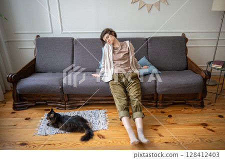 Weary apathetic woman lying still in relaxed pose while cat lying on floor, boredom and laziness 128412403