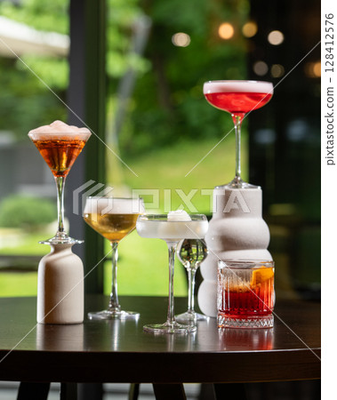 collection of five distinct alcoholic cocktails, varying in color and presentation, are artfully arranged on a dark table against a blurred background 128412576