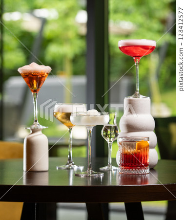 collection of five distinct alcoholic cocktails, varying in color and presentation, are artfully arranged on a dark table against a blurred background 128412577