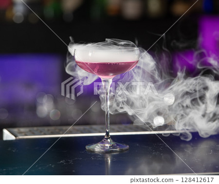 This visually striking pink alcoholic cocktail in a coupe glass features a large with more smoke billowing around it This visually striking pink alcoholic cocktail in a coupe glass features a large with more smoke billowing around it 128412617