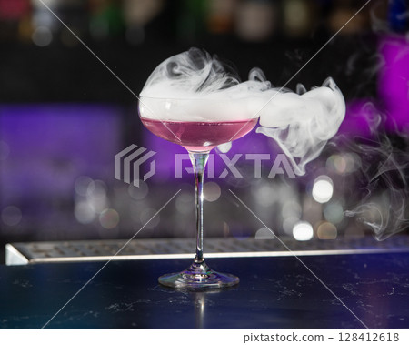 This visually striking pink alcoholic cocktail in a coupe glass features a large with more smoke billowing around it This visually striking pink alcoholic cocktail in a coupe glass features a large with more smoke billowing around it 128412618