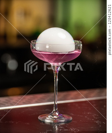 This visually striking pink alcoholic cocktail in a coupe glass features a large, dome-shaped smoke bubble on top, with more smoke billowing around it This visually striking pink alcoholic cocktail in a coupe glass features a large, dome-shaped smoke bubble on top, with more smoke billowing around it 128412621
