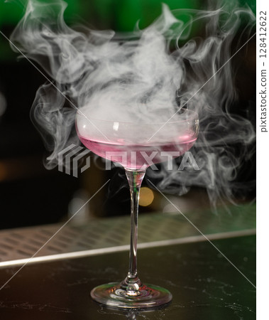 This visually striking pink alcoholic cocktail in a coupe glass features a large, dome-shaped smoke bubble on top, with more smoke billowing around it This visually striking pink alcoholic cocktail in a coupe glass features a large, dome-shaped smoke bubble on top, with more smoke billowing around it 128412622