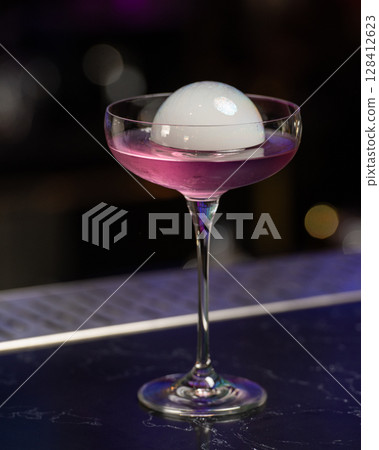 This visually striking pink alcoholic cocktail in a coupe glass features a large, dome-shaped smoke bubble on top, with more smoke billowing around it 128412623