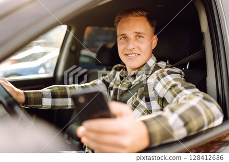 Man using smartphone while sitting in car parked in urban area during daytime. Lifestyle concept. 128412686