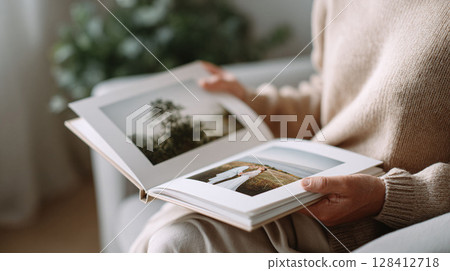 Woman reviewing a photo album, reliving memories. The image conveys nostalgia, remembrance, and the joy of looking back. Perfect for memory care, family, or lifestyle concepts. 128412718