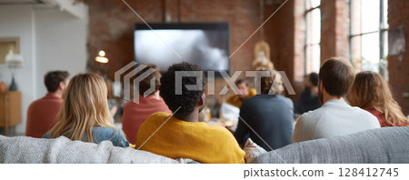 Friends gather, watching a screen. Group bonding, diverse faces, modern living. Implies community, leisure, entertainment. Good for social, media, tech themes. 128412745