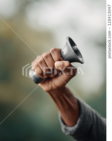 Close up of a raised fist holding a megaphone against a soft blurred background. Depicts power, voice, protest, activism, and advocacy. Perfect for social justice, marketing announcements. Close up of a raised fist holding a megaphone against a soft blurred background. Depicts power, voice, protest, activism, and advocacy. Perfect for social justice, marketing announcements. 128413047