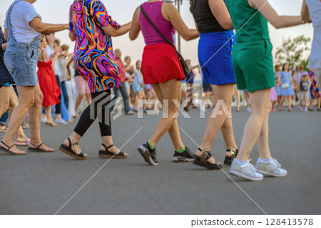 Diverse group of people dancing in colorful summer outfits outdoor , stepping in sync holding arms. Concept of dancing, joy, dancing, street event 128413578