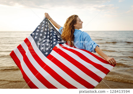 Young woman with American flag on beach. Patriotic holiday. Independence Day concept 128413594