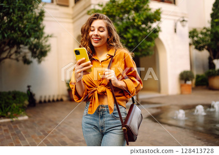 Young woman walking down street and using mobile phone. Business, technology, blogging concept. Young woman walking down street and using mobile phone. Business, technology, blogging concept. 128413728