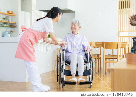 A female caregiver caring for a senior woman in the living room 128413746