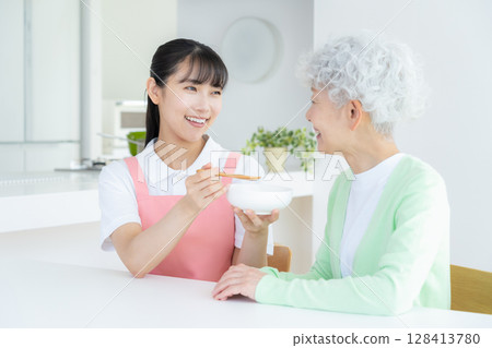 A female caregiver caring for a senior woman in the living room 128413780