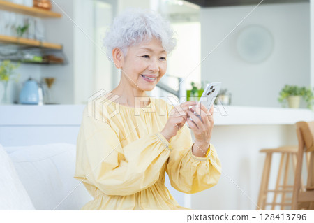 Senior woman looking at smartphone in living room 128413796