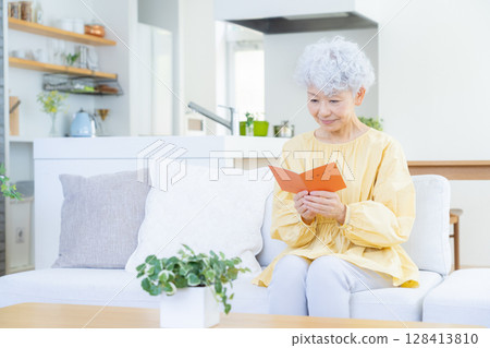 Senior woman looking at her pension book in the living room 128413810