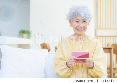 Senior woman looking at her savings passbook in the living room 128413812