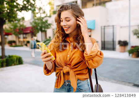 Young woman walking down street and using mobile phone. Business, technology, blogging concept. 128413849