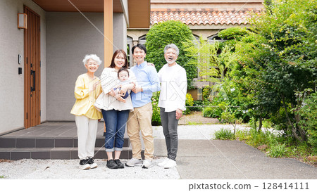 A three-generation family smiling and surrounding a baby in front of their house A three-generation family smiling and surrounding a baby in front of their house 128414111