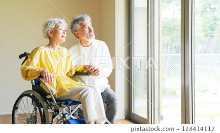 Senior man caring for a senior woman in a wheelchair 128414117