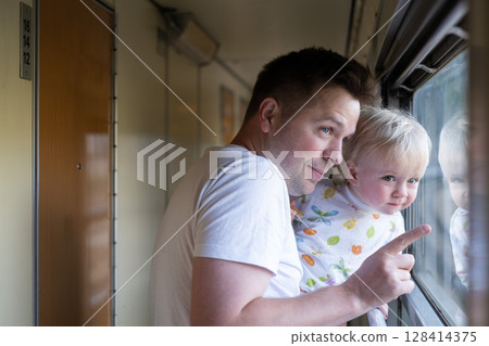 father, traveling with his little toddler by train, looking at the window.  128414375