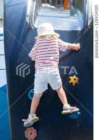 Toddler girl climbing up a slide on a playground 128414385
