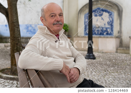 Elderly Spanish Man Sitting on a Bench in the Shade of Trees and Resting 128414469