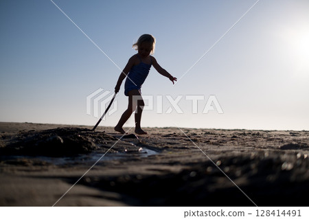 Little Girl Playing on the Beach with a Stick in the Sunset Light Little Girl Playing on the Beach with a Stick in the Sunset Light 128414491