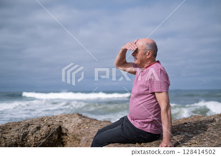 Elderly Man Sitting on the Beach and Looking at the Ocean, Remembering His Youth in Portugal 128414502