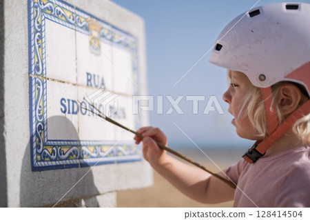 Little Girl in a Bike Helmet Learning to Read a Street Sign Little Girl in a Bike Helmet Learning to Read a Street Sign 128414504