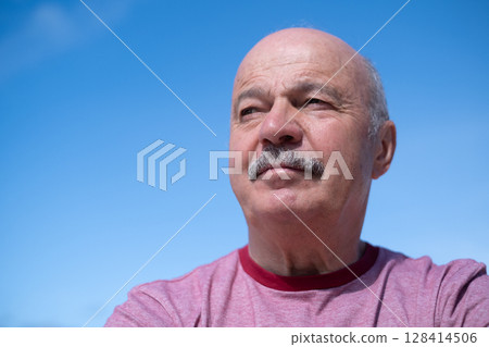 Elderly Spanish Man Against Blue Sky, Slightly Sad and Frowning Elderly Spanish Man Against Blue Sky, Slightly Sad and Frowning 128414506