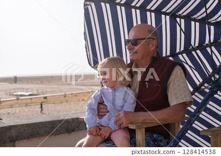 An elderly Spanish man sits with his granddaughter under a parasol on a promenade An elderly Spanish man sits with his granddaughter under a parasol on a promenade 128414538