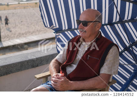 An elderly Spanish man sits under a sun umbrella on a promenade in a small Portuguese town  128414552