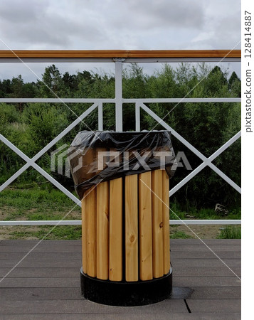 wooden trash bin on terrace overlooking green landscape on cloudy day. closeup. 128414887