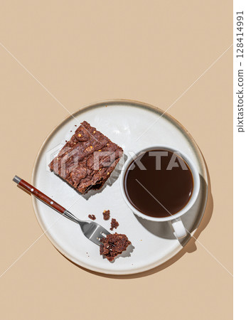 Chocolate brownie on a plate on a beige background with cup of freshly brewed coffee. 128414991